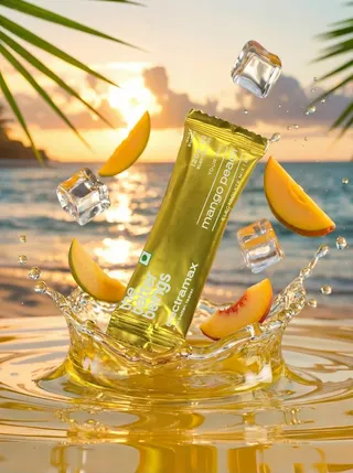 Gold mango-peach drink sachet bursting from a golden splash with ice cubes and peach slices on a sunset beach