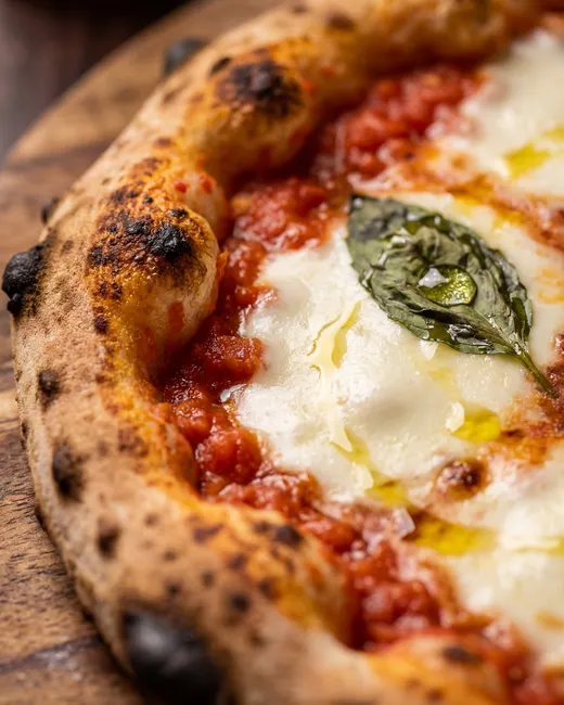 Close-up of a Neapolitan margherita pizza with blistered charred crust, molten mozzarella, basil and olive oil